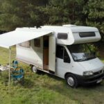 Zdjęcie Kampera Fiat Ducato II Dethleffs z rozłożoną markizą stojącego w lesie