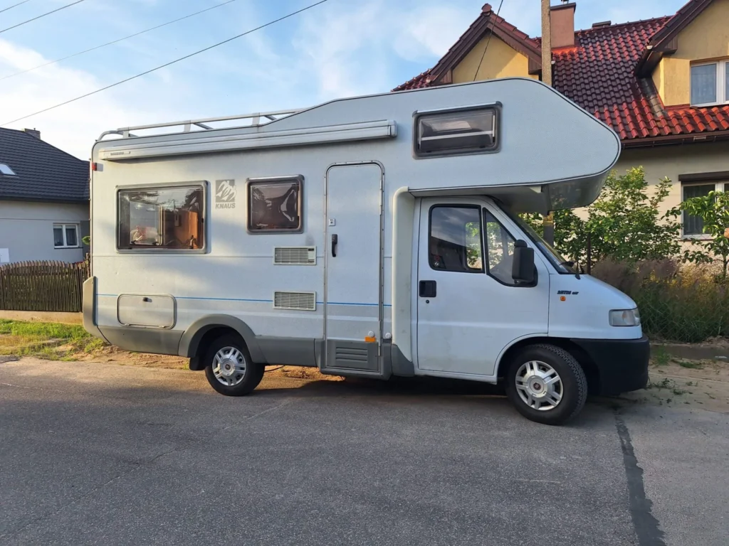 Kamper Fiat Ducato II "Knaus" na drodze w tle domy