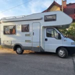 Kamper Fiat Ducato II "Knaus" na drodze w tle domy