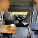 Wnętrze kampera na wynajem Hymer Koala, kokpit kierowcy i pasażera z widoczną alkową na górze