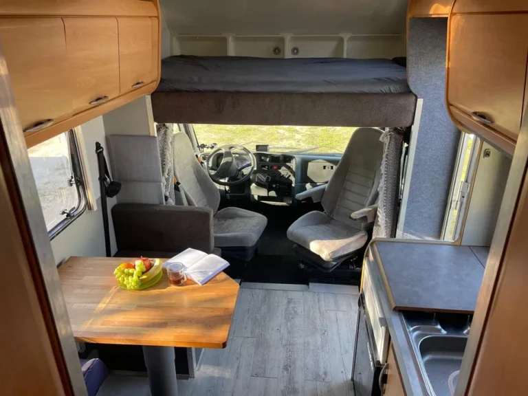 Wnętrze kampera na wynajem Hymer Koala, kokpit kierowcy i pasażera z widoczną alkową na górze