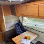 Wnętrze kampera na wynajem Hymer Koala, widać miejsca pasażerów, stoliki, okno boczne i górne szafki