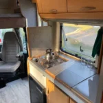 Wnętrze kampera na wynajem Hymer Koala widać okno, szafki górne i palnik gazowy